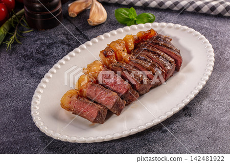 Sliced medium rare picanha steak on white plate with garlic and basil Sliced medium rare picanha steak on white plate with garlic and basil 142481922