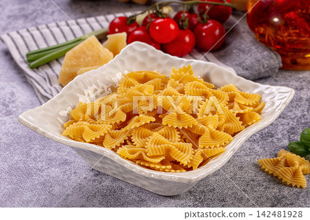 Dry farfalle pasta in white bowl with fresh ingredients for cooking Dry farfalle pasta in white bowl with fresh ingredients for cooking 142481928