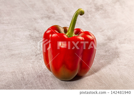 Single red bell pepper with green stem on a textured stone background Single red bell pepper with green stem on a textured stone background 142481940