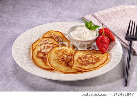 Homemade pancakes with sour cream, fresh strawberries, and mint on white plate 142481947