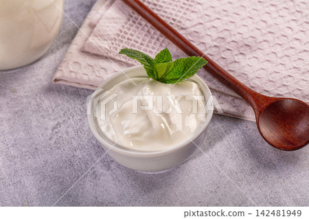 Creamy greek yogurt in white bowl with fresh mint sprig and wooden spoon on grey background Creamy greek yogurt in white bowl with fresh mint sprig and wooden spoon on grey background 142481949