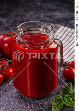Fresh tomato juice in glass mug with ripe tomatoes and basil on dark background Fresh tomato juice in glass mug with ripe tomatoes and basil on dark background 142481979