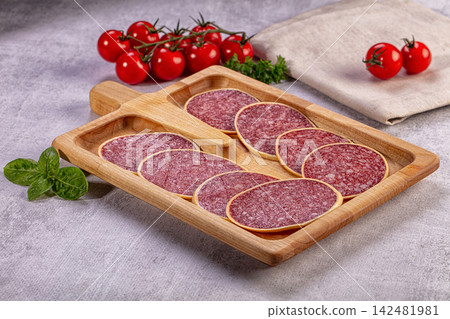 Sliced salami sausage on wooden tray with fresh cherry tomatoes and basil 142481981
