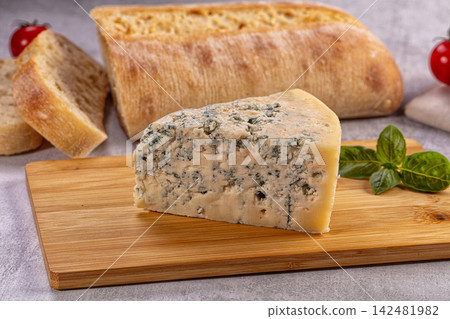 Wedge of blue cheese on wooden cutting board with fresh ciabatta bread and basil Wedge of blue cheese on wooden cutting board with fresh ciabatta bread and basil 142481982