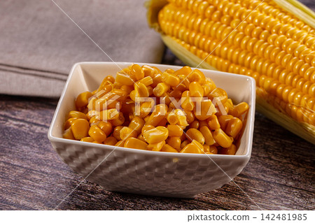 Sweet corn kernels in white bowl with fresh cob on wooden table Sweet corn kernels in white bowl with fresh cob on wooden table 142481985