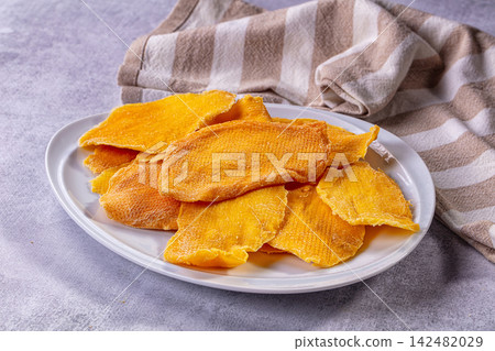 Dried mango slices served on white plate on grey textured background Dried mango slices served on white plate on grey textured background 142482029