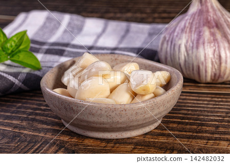 Marinated garlic cloves in a ceramic bowl on a rustic wooden table with fresh basil 142482032