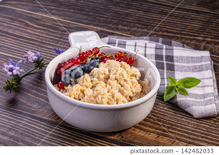 Oatmeal porridge with fresh blueberry and red currant in white bowl on dark wood table 142482033