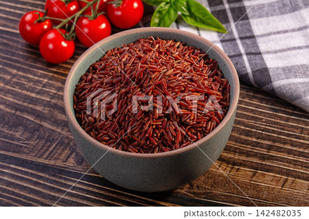 Bowl of raw red rice with cherry tomatoes and basil on wooden table 142482035