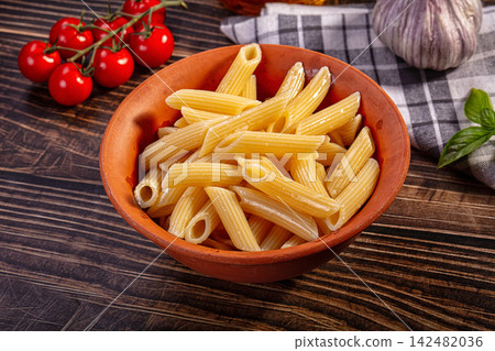 Cooked penne pasta in rustic terracotta bowl with fresh tomatoes and garlic on wooden table Cooked penne pasta in rustic terracotta bowl with fresh tomatoes and garlic on wooden table 142482036