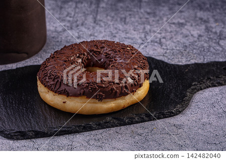 Chocolate donut with sprinkles on black slate platter against grey textured background Chocolate donut with sprinkles on black slate platter against grey textured background 142482040