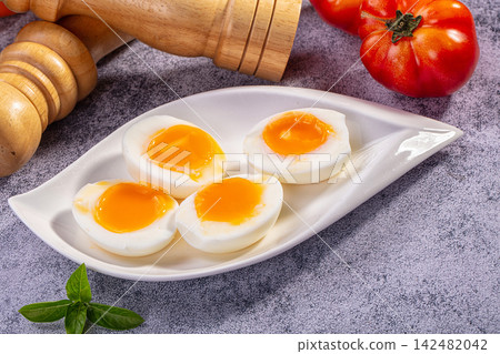 Soft boiled eggs with runny yolk on white plate with tomatoes and basil 142482042