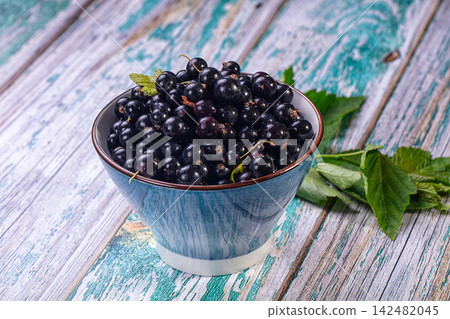 Fresh black currants in a blue ceramic bowl on rustic painted wood Fresh black currants in a blue ceramic bowl on rustic painted wood 142482045