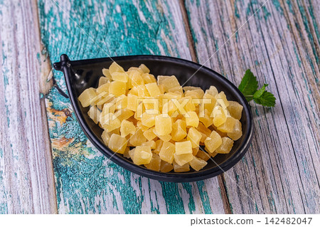 Dried pineapple cubes in a black bowl on a rustic wooden background Dried pineapple cubes in a black bowl on a rustic wooden background 142482047