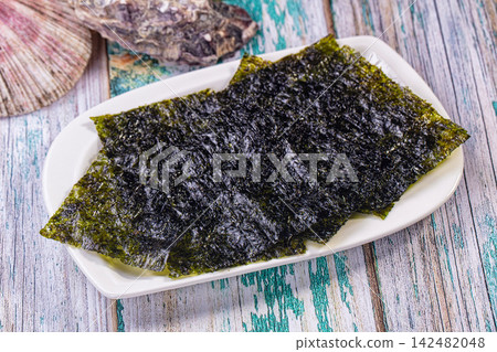 Crispy nori seaweed chips on white plate with seashells on rustic wooden table Crispy nori seaweed chips on white plate with seashells on rustic wooden table 142482048