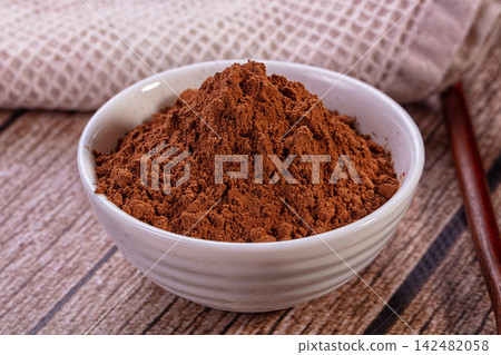 Cocoa powder in white ceramic bowl on rustic wooden surface 142482058