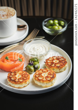 Savory Syrniki with Smoked Salmon, Olives and Sour Cream on White Plate 142482171