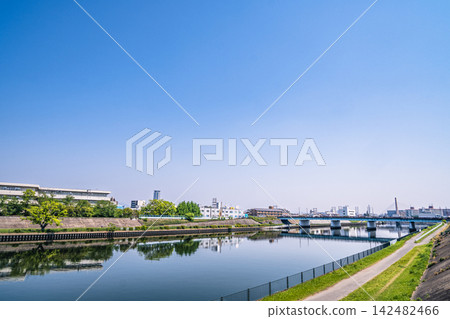 The scenery of the townscape and bridge reflected in the fresh greenery against the blue sky and on the river surface. The scenery of the townscape and bridge reflected in the fresh greenery against the blue sky and on the river surface. 142482466