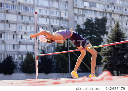 Female high jumper bends backward while clearing bar in close view Female high jumper bends backward while clearing bar in close view 142482479