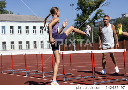 Teenage athlete practices high knee hurdle drill beside coach Teenage athlete practices high knee hurdle drill beside coach 142482497
