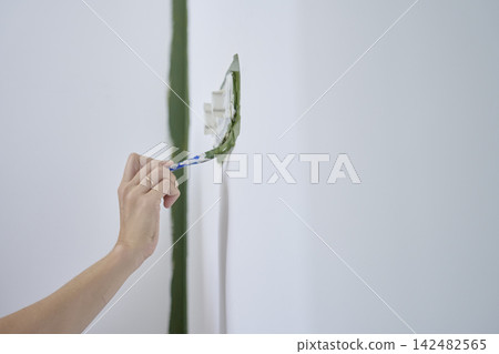 Hand brushing green paint along the edge of a covered wall outlet Hand brushing green paint along the edge of a covered wall outlet 142482565