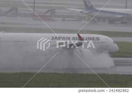 A passenger plane lands on a rainy runway, producing a plume of water from the engine's reverse thrust. A passenger plane lands on a rainy runway, producing a plume of water from the engine's reverse thrust. 142482862