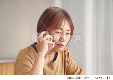 A senior woman clutches her smartphone and makes a phone call. A senior woman clutches her smartphone and makes a phone call. 142482913