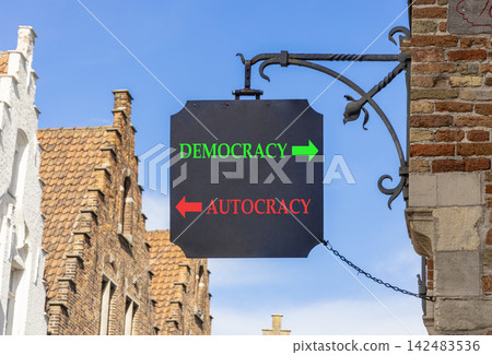 Democracy or autocracy words symbol. Concept words Democracy Autocracy on beautiful black road sign. Beautiful blue sky and Brugge street background. Business democracy autocracy concept. Copy space Democracy or autocracy words symbol. Concept words Democracy Autocracy on beautiful black road sign. Beautiful blue sky and Brugge street background. Business democracy autocracy concept. Copy space 142483536