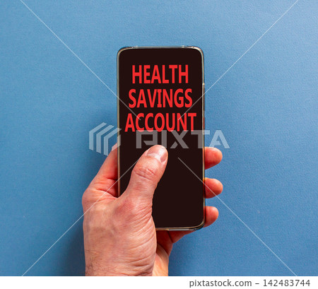 Health saving account symbol. Concept words Health saving account on beautiful mobile phone screen. Beautiful blue background. Businessman hand. Medical Health saving account concept. Copy space. Health saving account symbol. Concept words Health saving account on beautiful mobile phone screen. Beautiful blue background. Businessman hand. Medical Health saving account concept. Copy space. 142483744