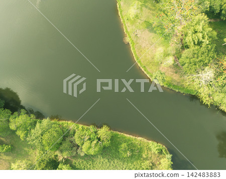 Drone view of curving lake water framed by green shoreline in tropical landscape. Water sustainability, conservation, ecosystem care, and nature themes. Environmental conservation. Land management. Drone view of curving lake water framed by green shoreline in tropical landscape. Water sustainability, conservation, ecosystem care, and nature themes. Environmental conservation. Land management. 142483883