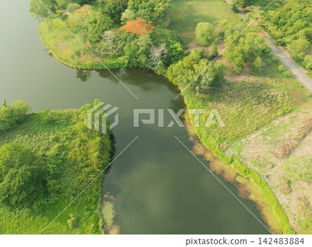 Aerial view of tranquil retreat resort garden and lake surrounded by trees. Peaceful wellness destination in tropical nature for relaxation, travel and eco tourism. Nature escape, sustainable tourism. Aerial view of tranquil retreat resort garden and lake surrounded by trees. Peaceful wellness destination in tropical nature for relaxation, travel and eco tourism. Nature escape, sustainable tourism. 142483884