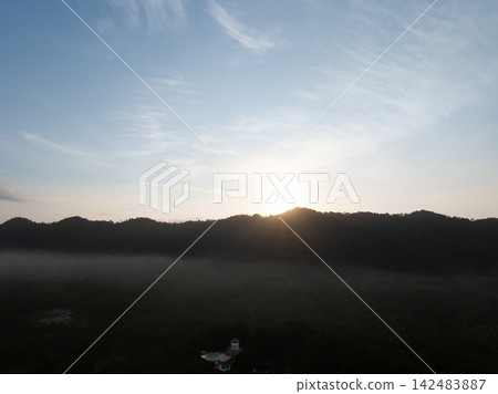 Sunrise over a misty tropical mountain forest with morning fog. Natural landscape with expansive sky for travel and environmental themes. Nature, tourism and conservation. Climate, ecology concepts. Sunrise over a misty tropical mountain forest with morning fog. Natural landscape with expansive sky for travel and environmental themes. Nature, tourism and conservation. Climate, ecology concepts. 142483887