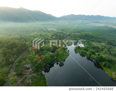 Aerial view of peaceful retreat resort surrounded by tropical forest, lake and misty mountain valley at sunrise. Wellness tourism, nature escape and eco travel. Ecotourism and healthy travel. Aerial view of peaceful retreat resort surrounded by tropical forest, lake and misty mountain valley at sunrise. Wellness tourism, nature escape and eco travel. Ecotourism and healthy travel. 142483888