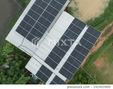 Top down aerial view of rooftop solar panels on a rural farm building beside water ponds and green vegetation, generating renewable electricity for sustainable agriculture and clean energy production. Top down aerial view of rooftop solar panels on a rural farm building beside water ponds and green vegetation, generating renewable electricity for sustainable agriculture and clean energy production. 142483900