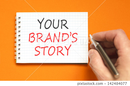Branding and your brands story symbol. Concept words Your brands story on beautiful white note. Beautiful orange background. Businessman hand. Business branding your brands story concept. Copy space. Branding and your brands story symbol. Concept words Your brands story on beautiful white note. Beautiful orange background. Businessman hand. Business branding your brands story concept. Copy space. 142484077