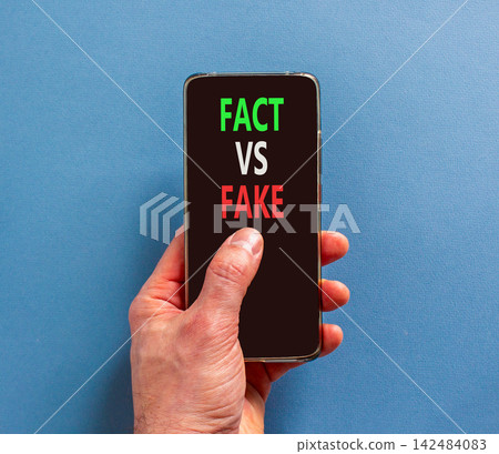 Fact vs versus fake words symbol. Concept words Fact vs Fake on beautiful mobile phone screen. Beautiful blue background. Businessman hand. Business and fact vs versus fake concept. Copy space. Fact vs versus fake words symbol. Concept words Fact vs Fake on beautiful mobile phone screen. Beautiful blue background. Businessman hand. Business and fact vs versus fake concept. Copy space. 142484083