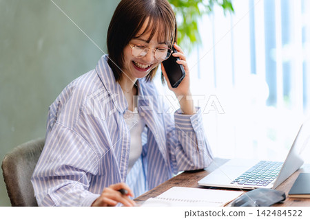 A young woman with a smile happily talking on her smartphone and a laptop. A young woman with a smile happily talking on her smartphone and a laptop. 142484522