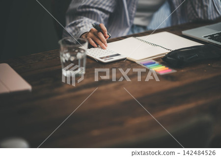 一隻手一邊用計算機計算，一邊在筆記本上做筆記。 142484526