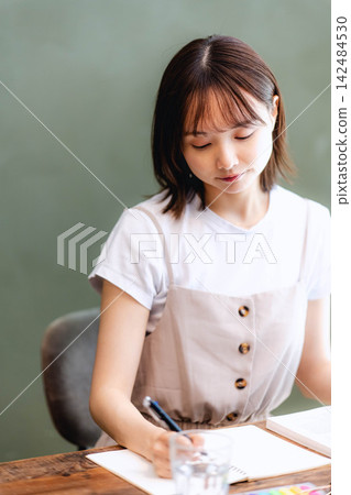 一位年輕的日本女性在咖啡館學習,並做筆記。 一位年輕的日本女性在咖啡館學習,並做筆記。 142484530