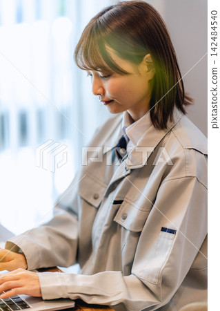 一位身穿工作服的年輕女工正在使用筆記型電腦工作。 一位身穿工作服的年輕女工正在使用筆記型電腦工作。 142484540