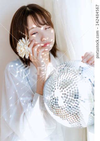 A woman in a white blouse with a white flower behind her ear and a gentle expression. A woman in a white blouse with a white flower behind her ear and a gentle expression. 142484567