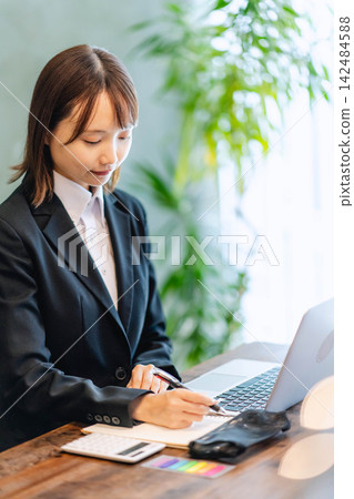 一位身穿職業套裝的年輕女子正在筆記本上做筆記。 一位身穿職業套裝的年輕女子正在筆記本上做筆記。 142484588