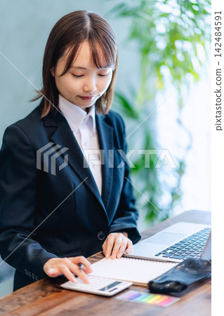 A young woman in a suit using a calculator to perform calculations. A young woman in a suit using a calculator to perform calculations. 142484591