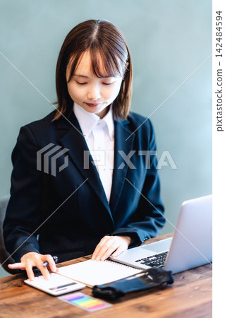 一位身穿西裝的年輕女子正在用計算機核對文件。 一位身穿西裝的年輕女子正在用計算機核對文件。 142484594