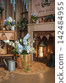 Cozy spring corner by the fireplace with a basket of blue flowers and a watering can 142484955