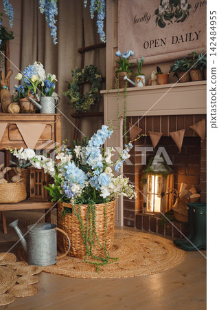 Cozy spring corner by the fireplace with a basket of blue flowers and a watering can Cozy spring corner by the fireplace with a basket of blue flowers and a watering can 142484955