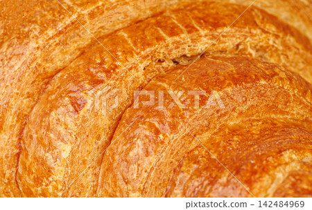 Mouth-watering golden croissant crust close up. Freshly baked artisan pastry with flaky texture. Mouth-watering golden croissant crust close up. Freshly baked artisan pastry with flaky texture. 142484969