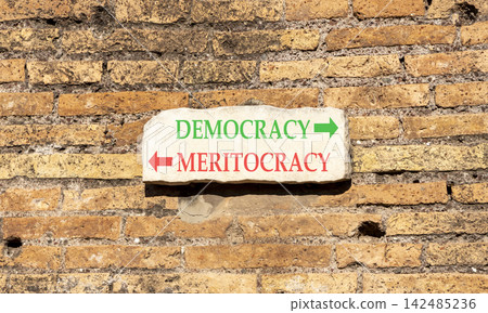 Democracy or meritocracy words symbol. Concept words Democracy Meritocracy on beautiful white sign plate. Beautiful brick wall background. Business democracy meritocracy concept. Copy space Democracy or meritocracy words symbol. Concept words Democracy Meritocracy on beautiful white sign plate. Beautiful brick wall background. Business democracy meritocracy concept. Copy space 142485236