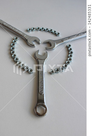 Mechanical concept with shiny hand wrenches inside a circle of metal nuts isolated on white Mechanical concept with shiny hand wrenches inside a circle of metal nuts isolated on white 142485331