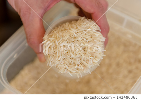 Scooping basmati rice with a measuring cup; the hands measuring long-grain rice; the image of Indian cuisine and ethnic cooking ingredients. Scooping basmati rice with a measuring cup; the hands measuring long-grain rice; the image of Indian cuisine and ethnic cooking ingredients. 142486363